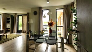 A modern dining area with a glass table, metal chairs, and a vase of dried flowers.