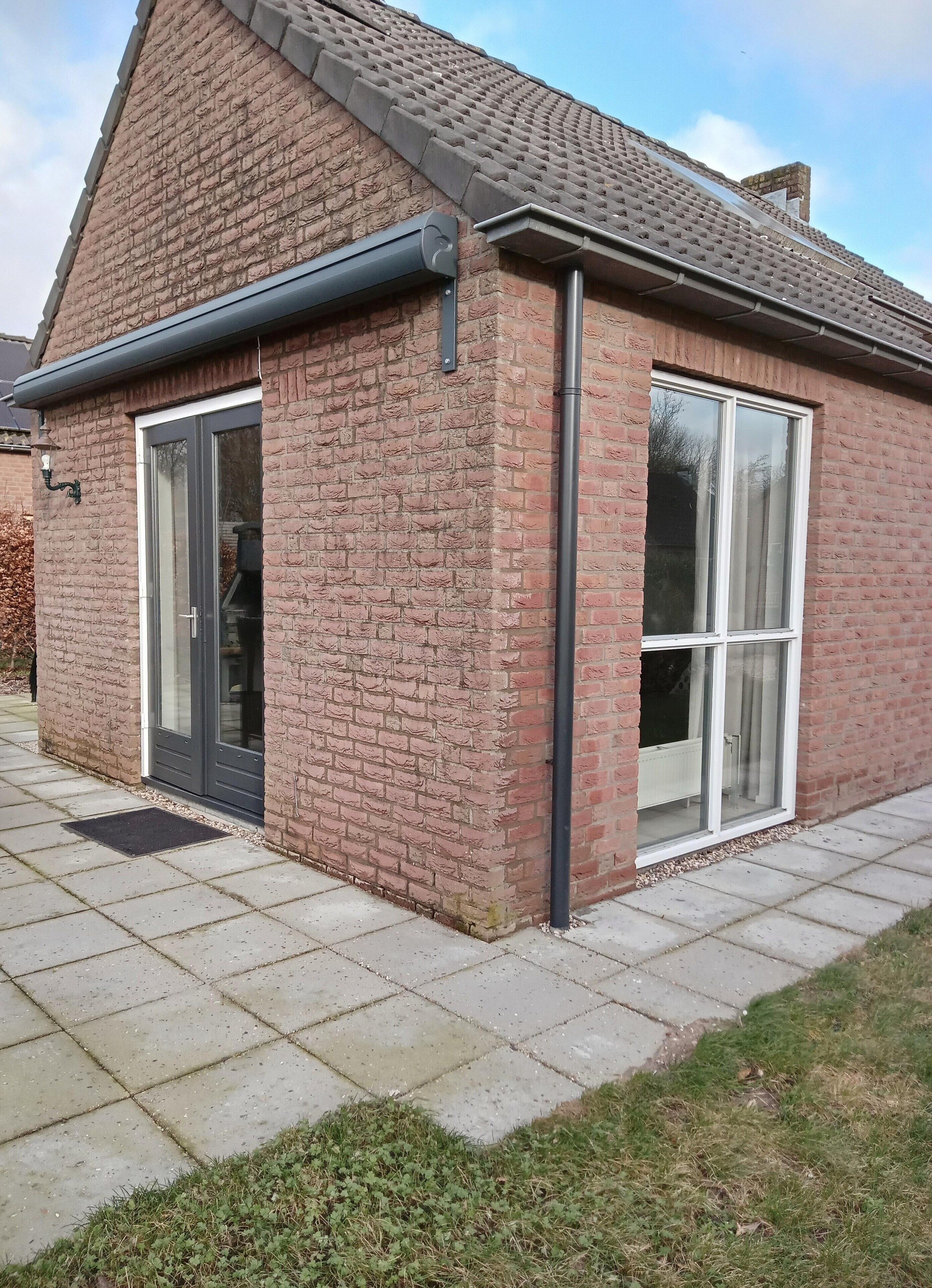 A brick house with a tiled roof, a large sliding glass door, and a small attached garage.