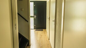 A hallway with wooden flooring, a staircase, and a door leading to another room.