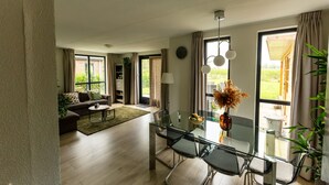 A modern living room with a glass dining table, a sofa, and a large window with curtains.