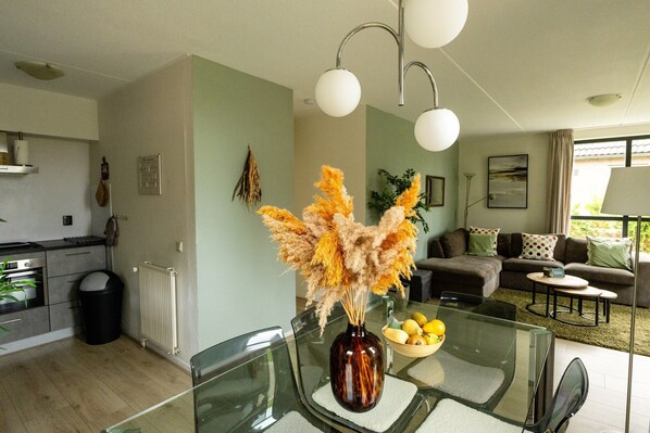 A modern kitchen with a dining area, a living room with a sofa and a coffee table, and a vase with dried flowers on the dining table.