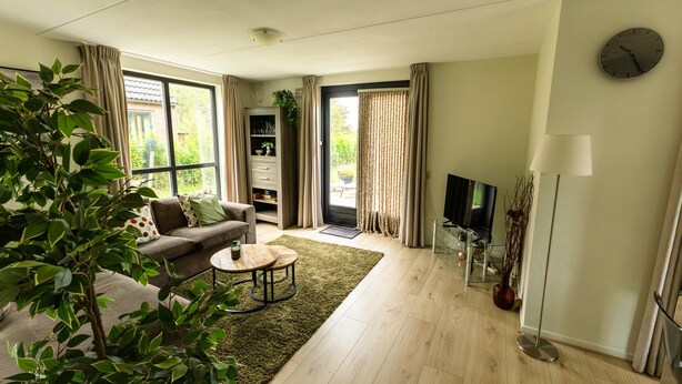 A modern living room with a sofa, coffee table, and a TV. There is a bookshelf and a plant in the corner.