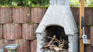 A stone-built outdoor oven with a fire inside, surrounded by a brick wall and greenery. - Cosy Holiday Home Yalet in Brilon-wald (Brilon)