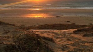 Uma praia com o sol se pondo sobre o oceano.
