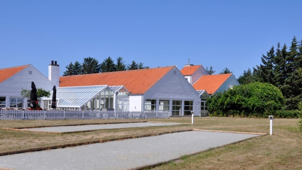 Um edifício com telhado vermelho e paredes brancas, uma área cercada com superfície pavimentada e um campo gramado.