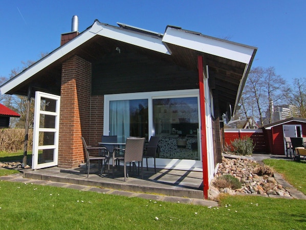 A modern house with a sloped roof, a brick chimney, and a glass door leading to a patio with outdoor furniture. - Inviting log House With 2 Terraces and Cozy Fireplace in Damp (Damp)