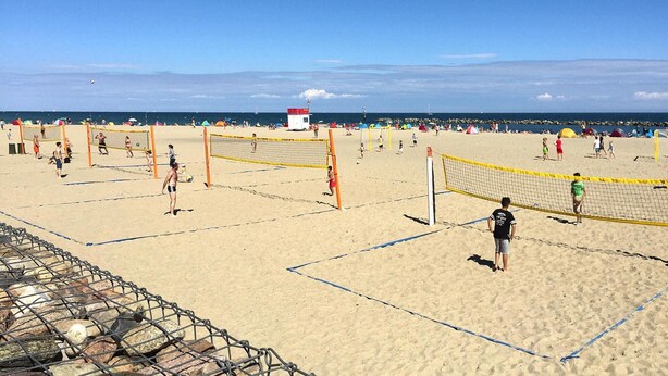 Een beachvolleybalveld met netten en een uitkijktoren op de achtergrond.