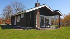 Een modern huis met een gevel van baksteen, een grote glazen deur en een overdekte veranda met tuinmeubilair.