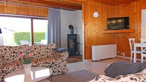 Een gezellig interieur van een chalet met een bank, een kleine tafel met een vaas, een open haard, een aan de muur bevestigde televisie en een eethoek.