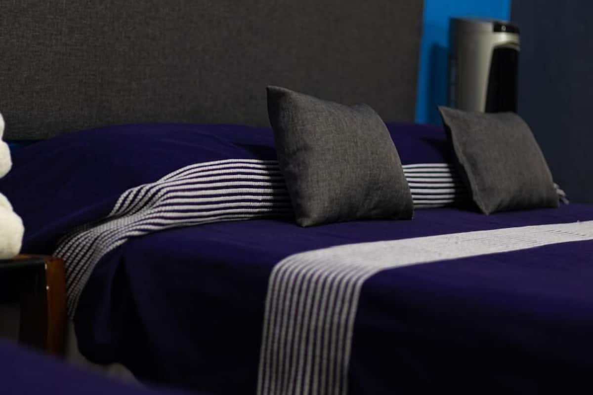A neatly made bed with striped bedding and two pillows, a dark headboard, and a speaker in the background.