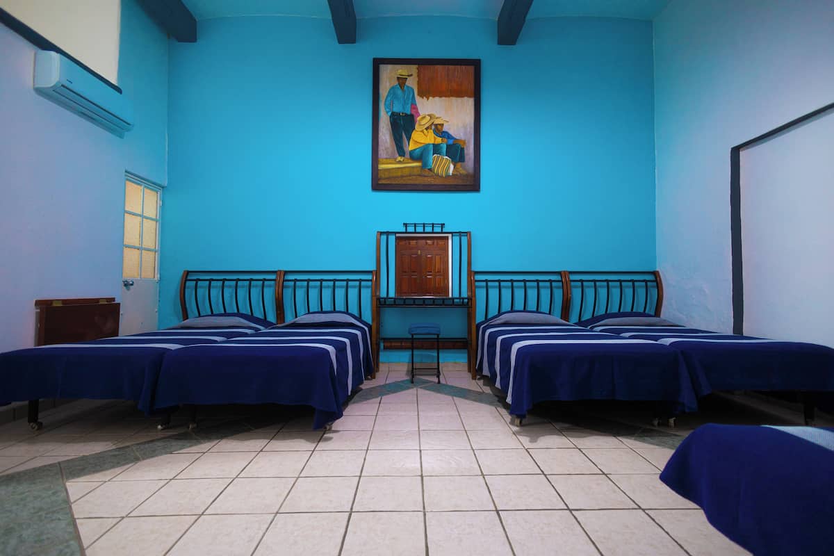 A room with four beds aligned in a row, a wooden cabinet, and a painting on the wall.