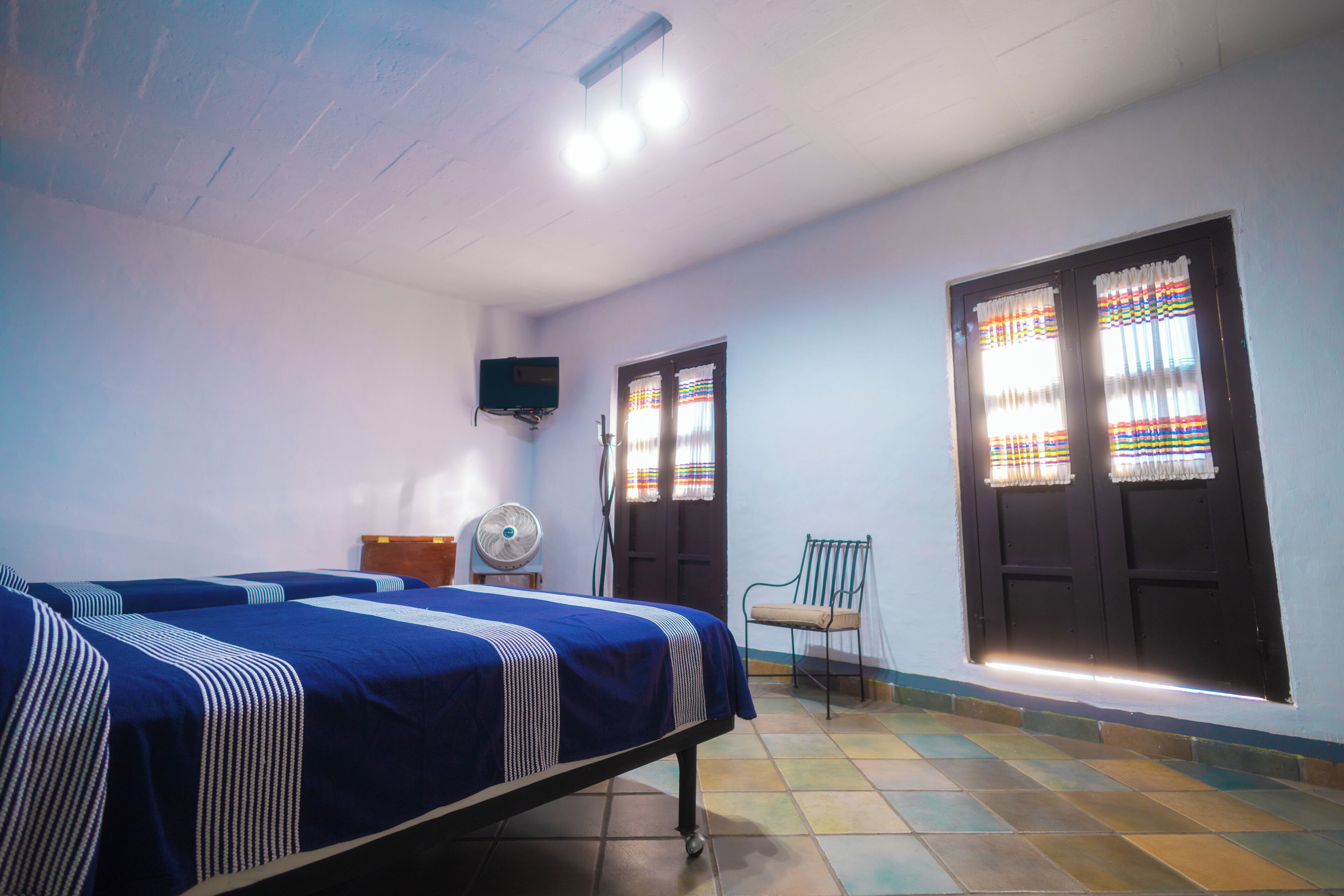 Une chambre avec deux lits, un ventilateur, une télévision et une fenêtre avec des rideaux.