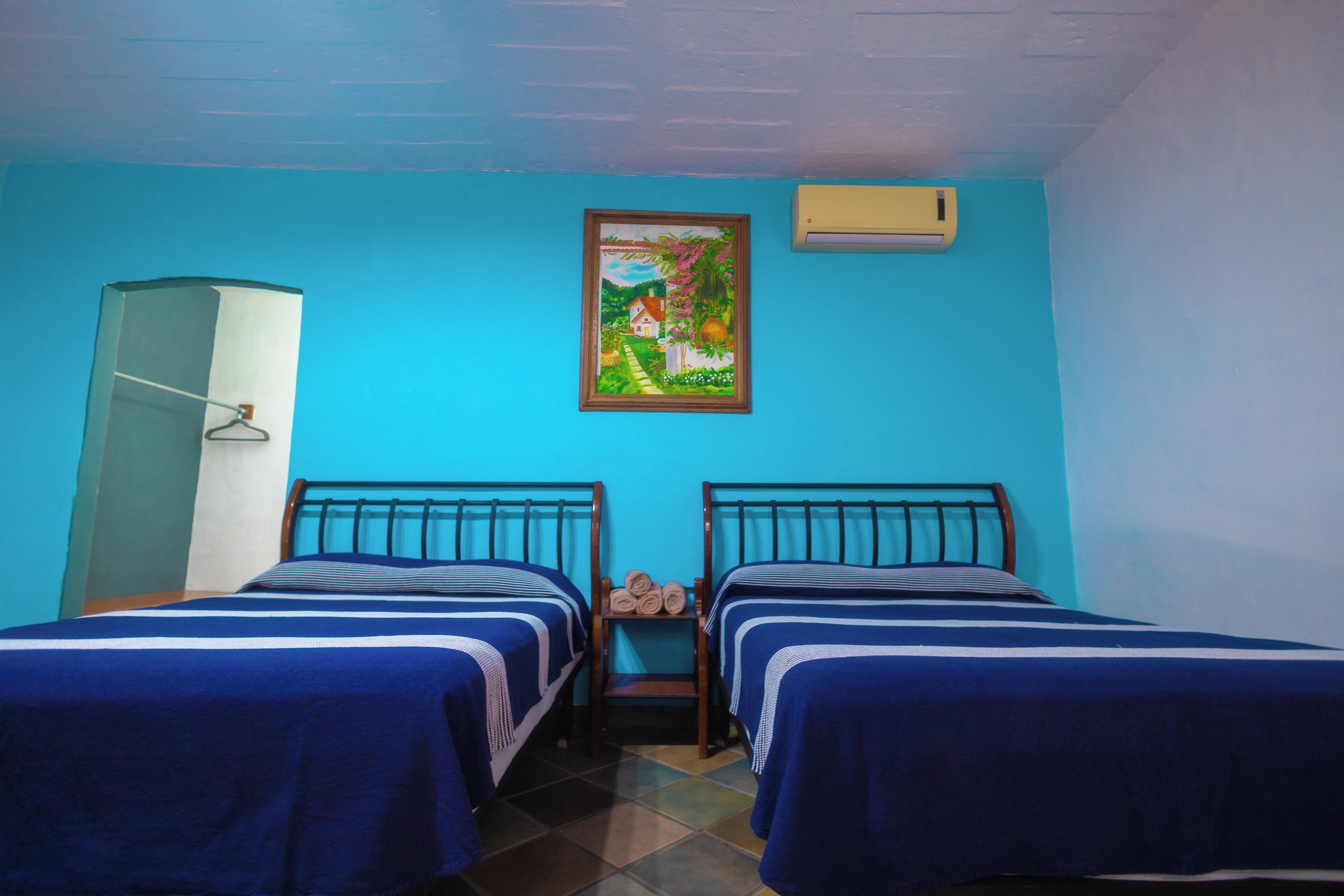 Una habitación con dos camas, un armario, un cuadro y un aire acondicionado.