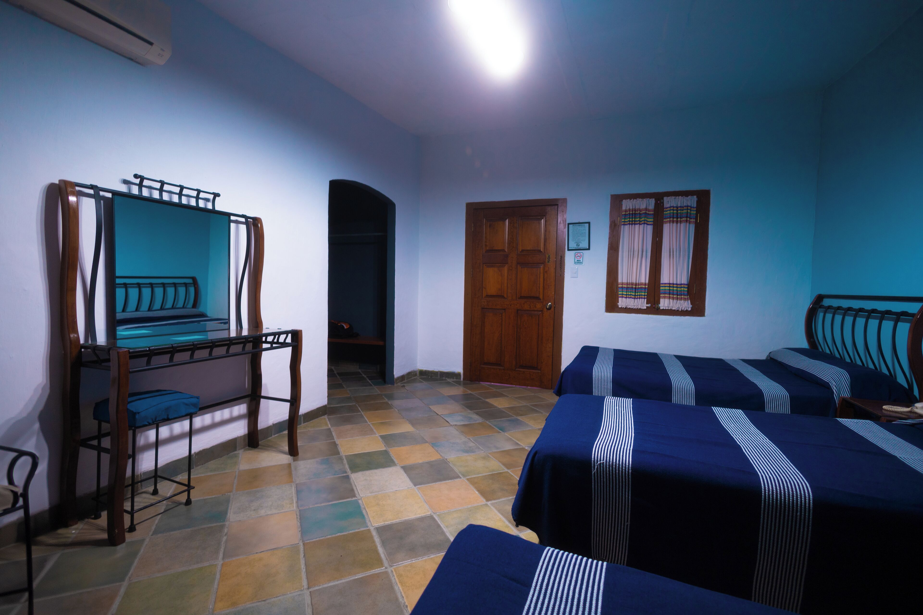 Una habitación con dos camas, un banco de madera, un espejo y piso de baldosas.