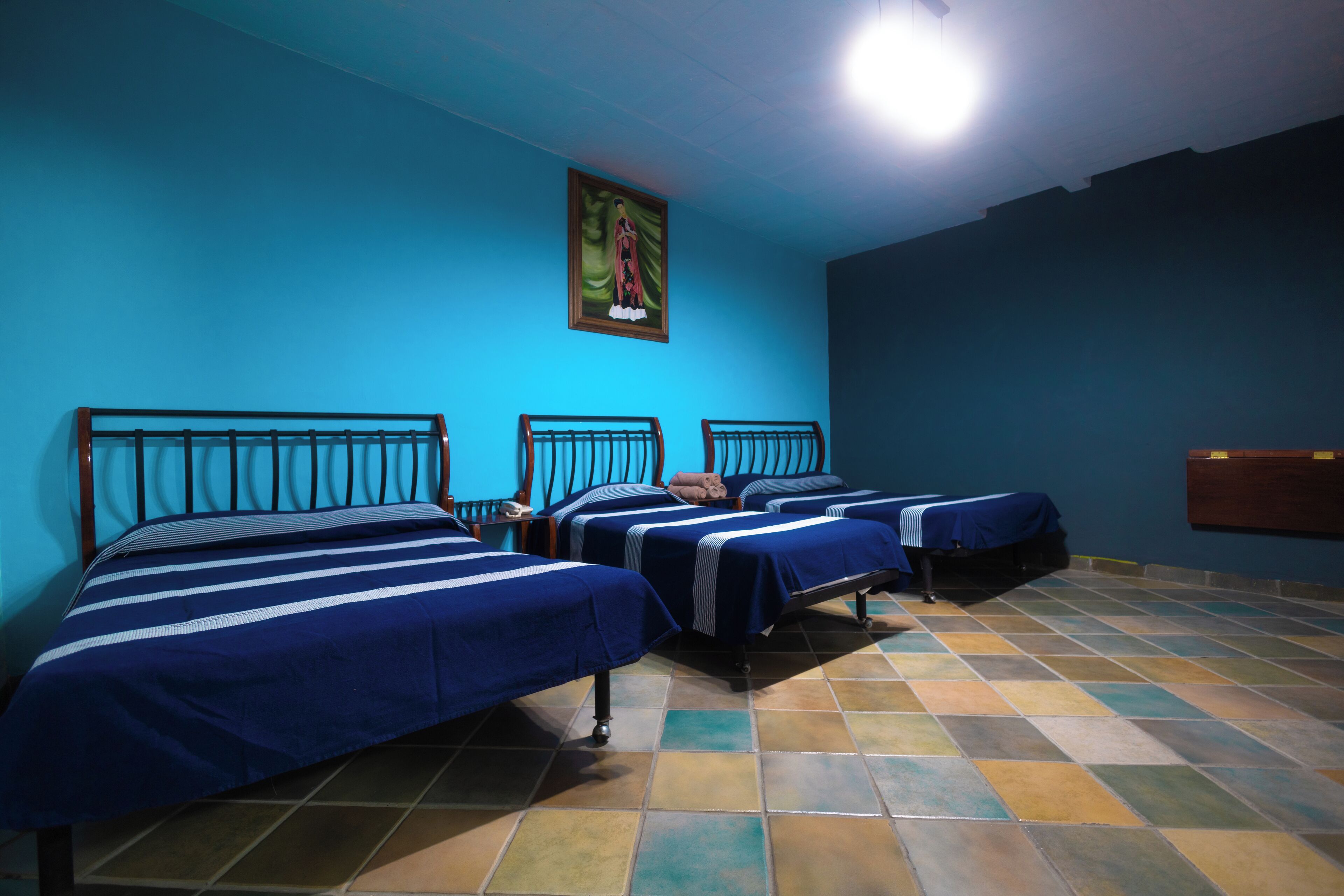 Een kamer met drie bedden, een blauwe muur en een betegelde vloer.