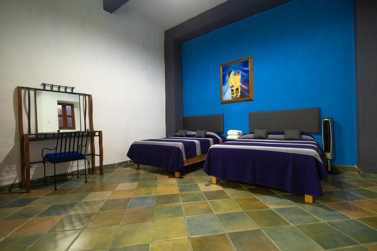 Una habitación de hotel con dos camas, un escritorio, una silla y un cuadro grande en la pared.