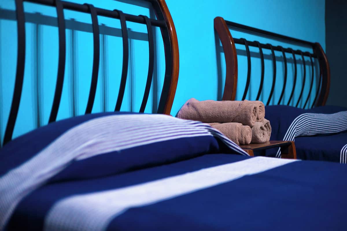 A neatly made bed with blue and white striped bedding, a wooden headboard, and a pair of folded towels on a wooden nightstand.
