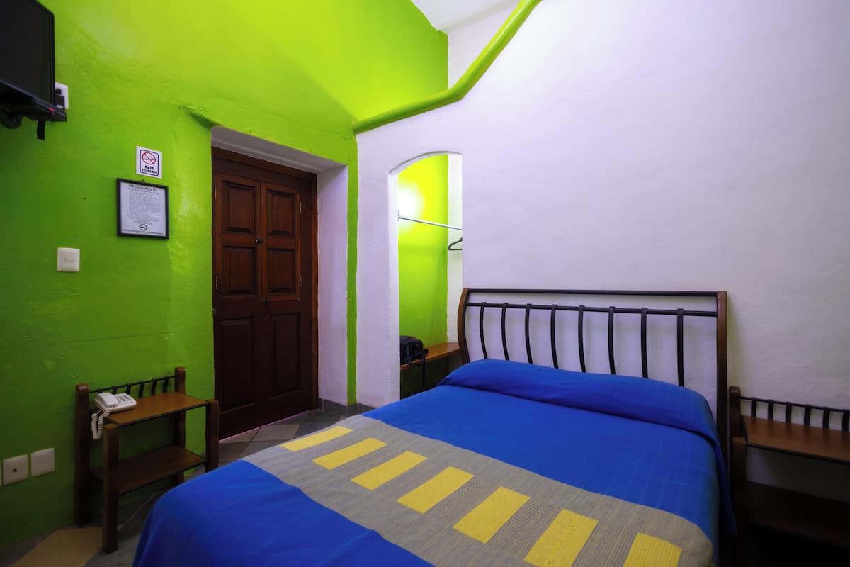 A room with a bed, a wooden chair, a small table, and a door.