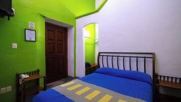 Una habitación con una cama, una silla de madera, una mesita y una puerta.