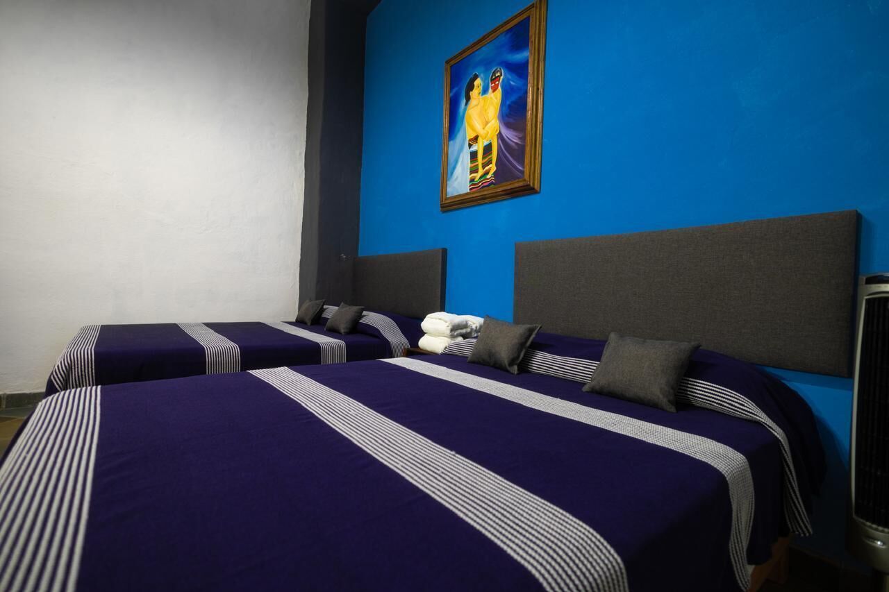 A hotel room with two beds, each with striped bedding and pillows, a blue accent wall, and a framed picture above the beds.