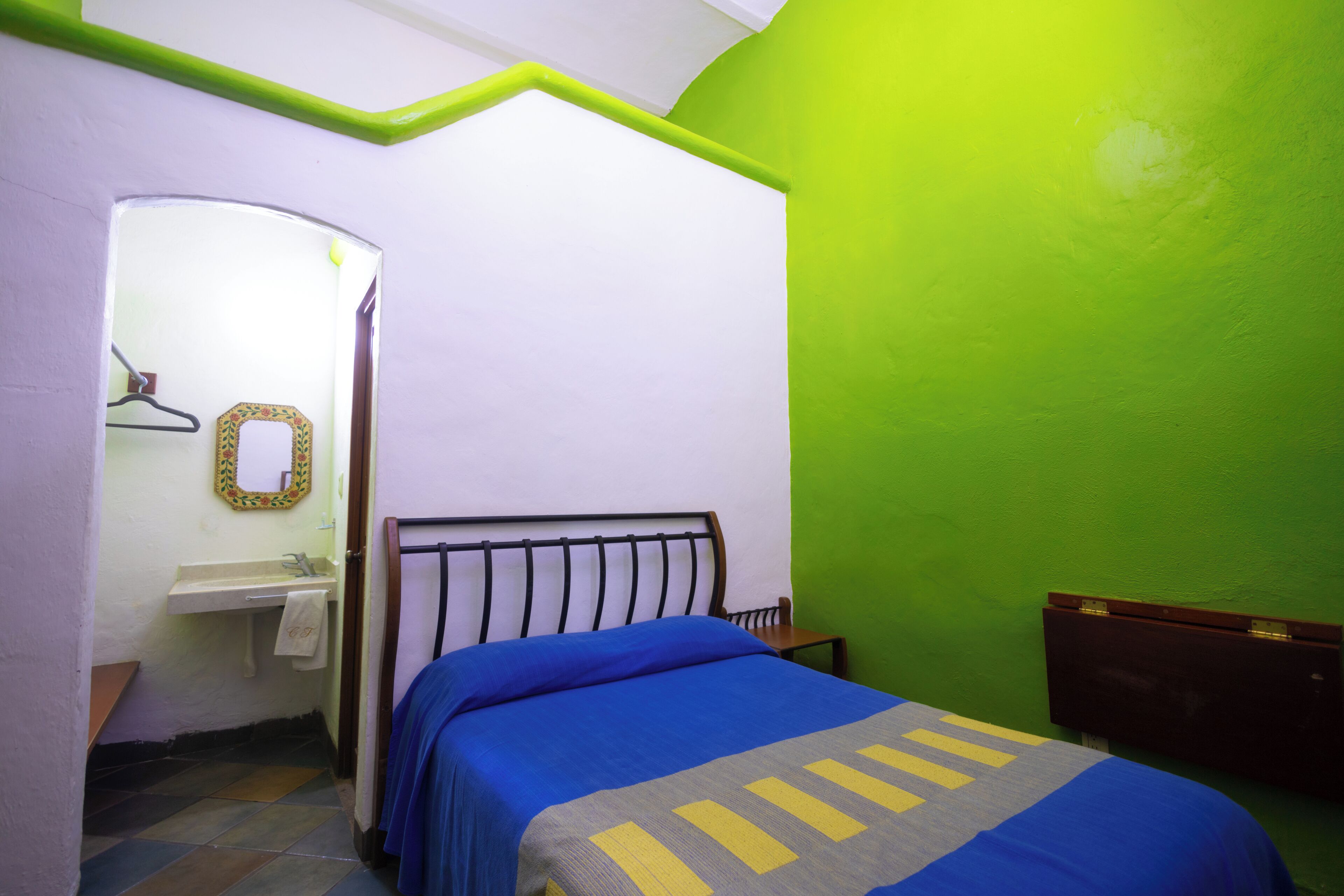 A small, brightly colored room with a bed, a small sink, and a mirror.