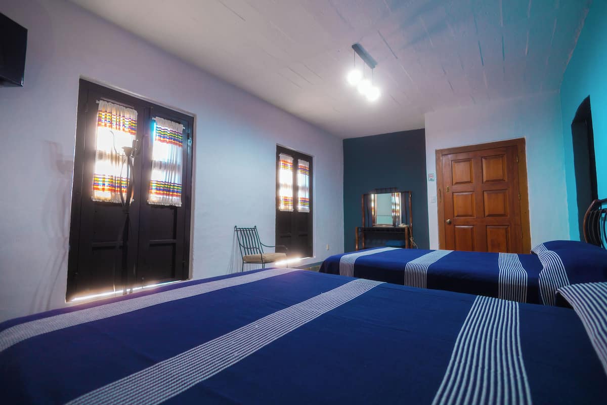 A room with three beds, a wooden door, and a chair.