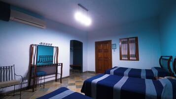 A room with four beds, a wooden bench, a door, and a window with curtains.