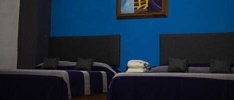 Quarto de hotel com duas camas, uma parede azul e um quadro emoldurado.