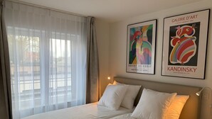 Une chambre d’hôtel avec un lit, des rideaux blancs et deux œuvres d’art encadrées accrochées au mur.