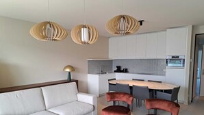Un salon moderne avec un canapé, une table basse et un coin repas avec des chaises. Des lampes suspendues sont placées au-dessus de la table à manger.