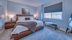 A bedroom with a bed, bedside tables, a bench, a window with blinds, and a painting on the wall. - -:- Cowboy Casa -:- Modern New Construction - 3BR+  (Cody)