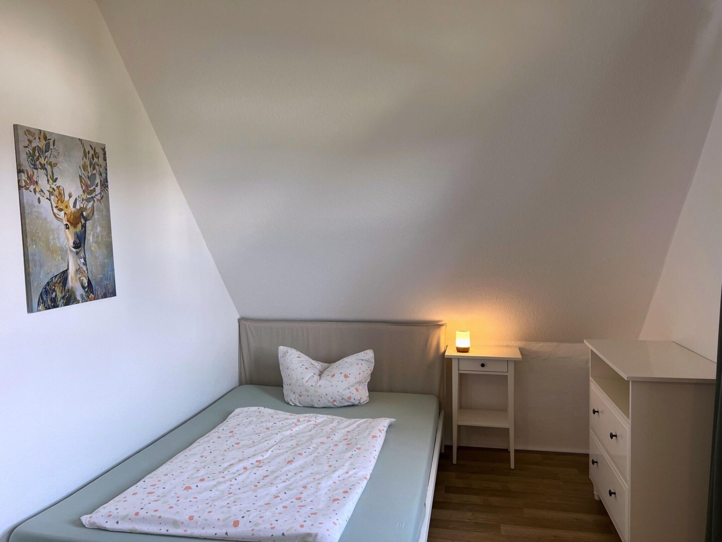 Een kleine, netjes ingerichte slaapkamer met een enkel bed, een nachtkastje met een lamp en een kledingkast.