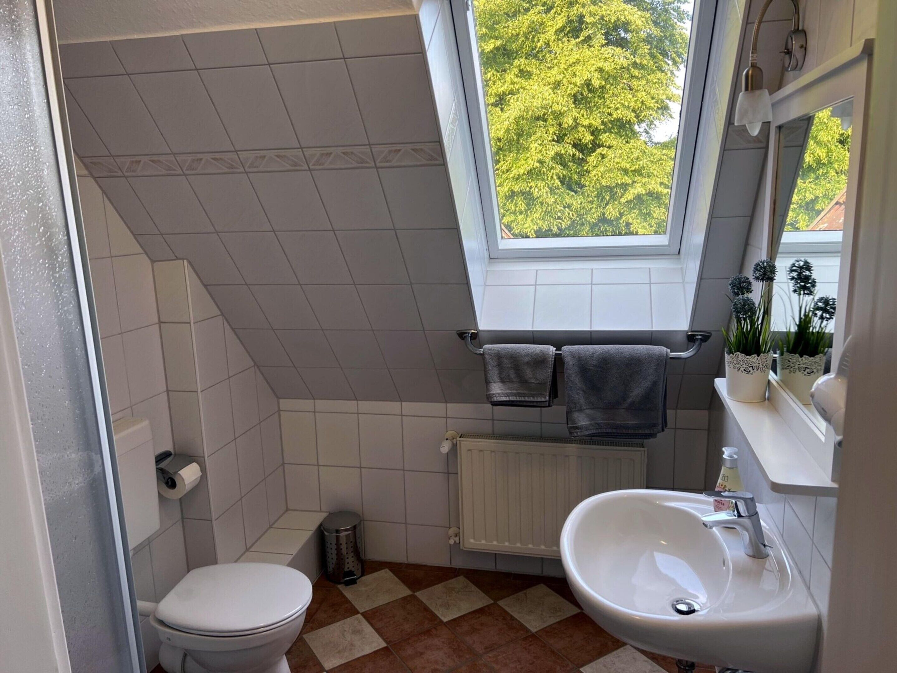Une salle de bain équipée de toilettes, d’un lavabo et d’une fenêtre donnant sur des arbres.