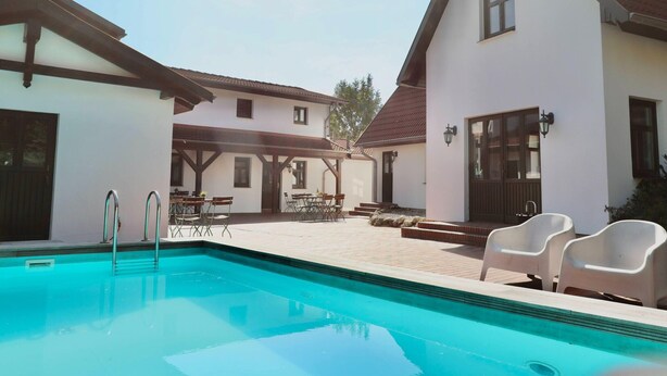 A pool area with a clear blue pool, white buildings with dark trim, and outdoor seating. - Studio in Dargun With Pool Near Lake Kummerow (Dargun)