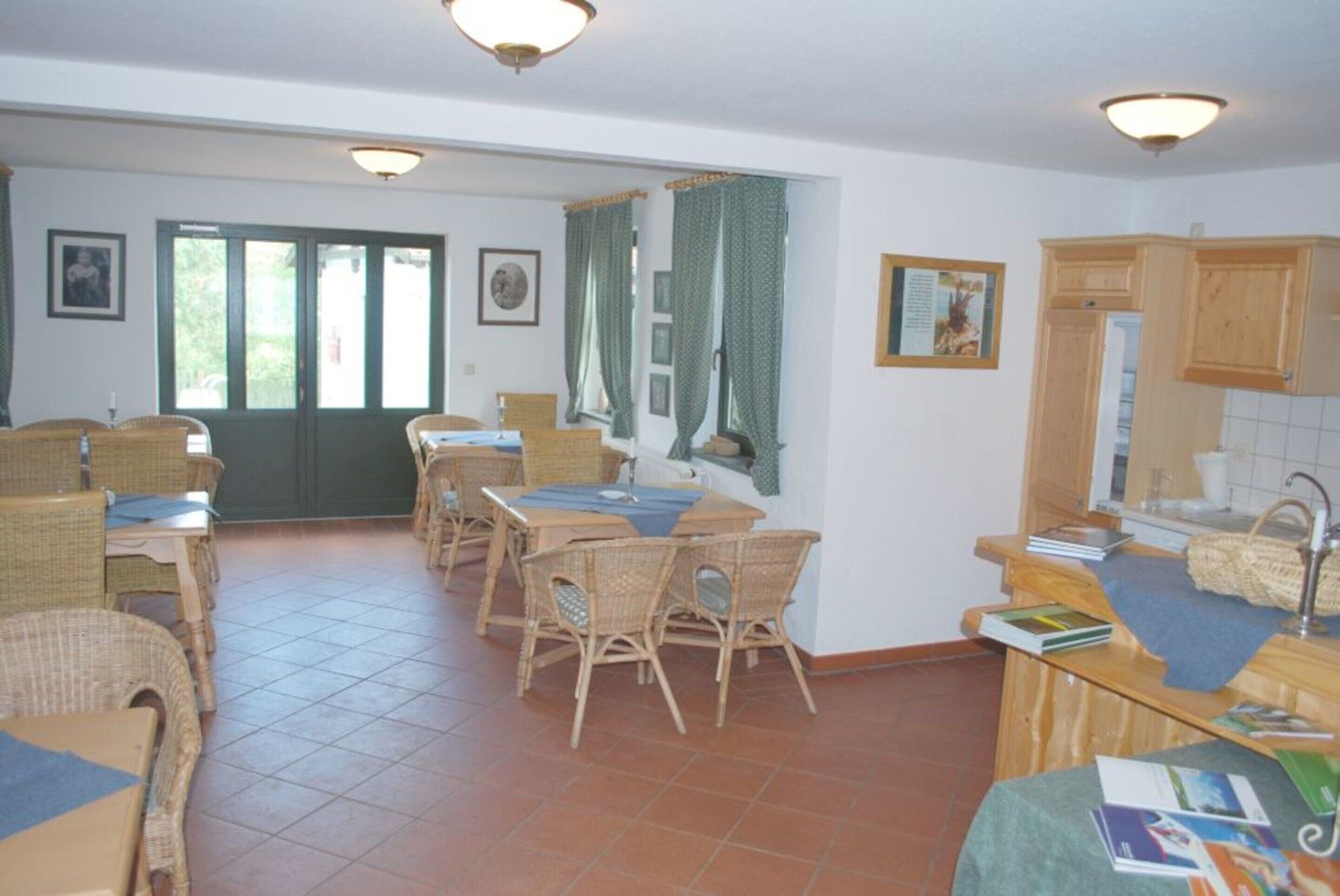 Zona pranzo con mobili in vimini, pavimento piastrellato e cucina con pensili in legno.