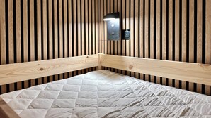 Ein Etagenbett mit einer gesteppten Matratze in einem Raum mit Holzboden und einer an der Wand befestigten Lampe.