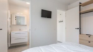 Une chambre à coucher comprenant un lit, un téléviseur fixé au mur, une armoire et une salle de bain avec un miroir et un porte-serviettes.