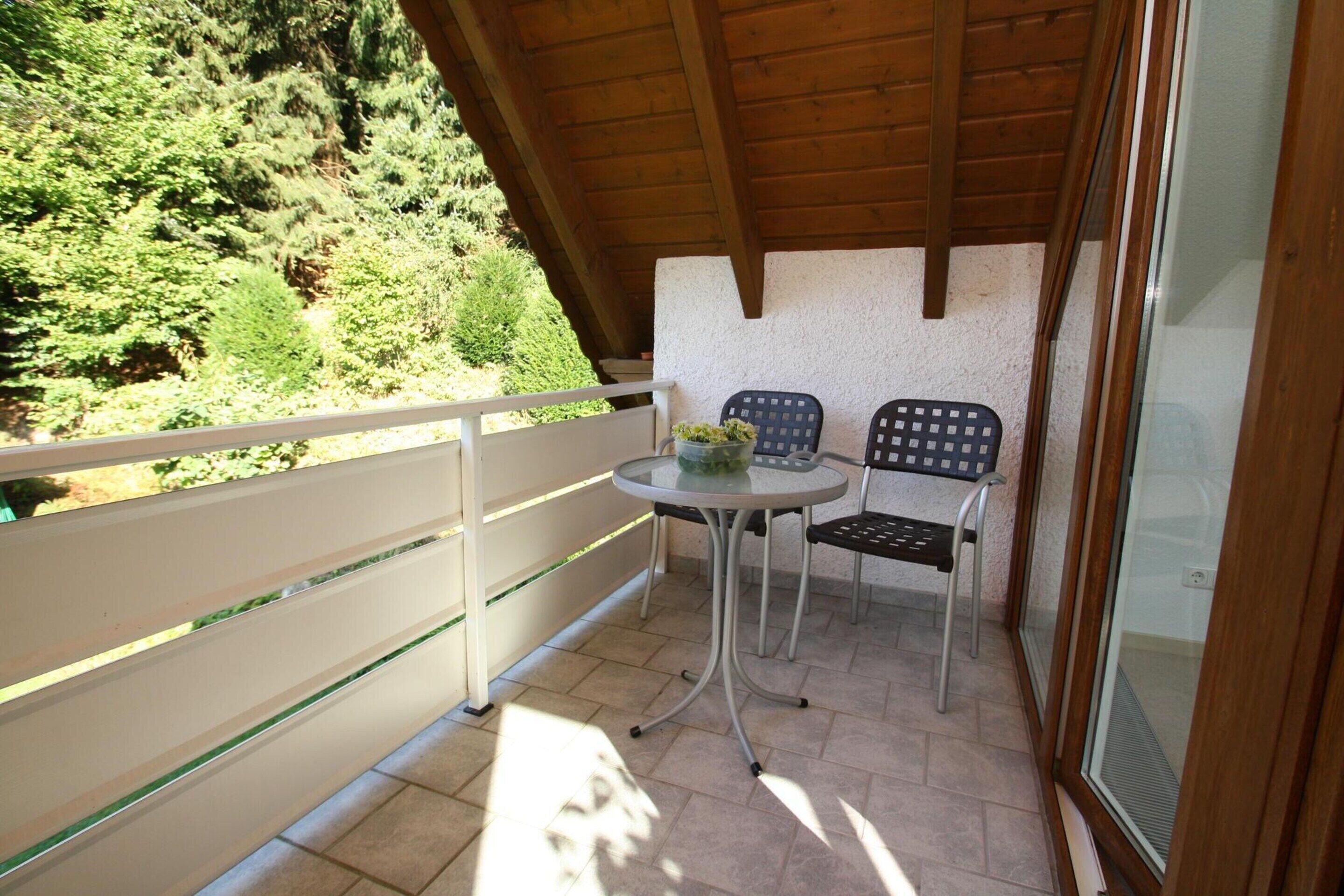 Un balcon doté d’un plafond en bois, de deux chaises, d’une petite table ronde et d’une porte vitrée.