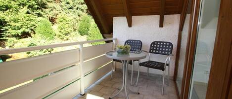 Un balcon doté d’un plafond en bois, de deux chaises, d’une petite table ronde et d’une porte vitrée.