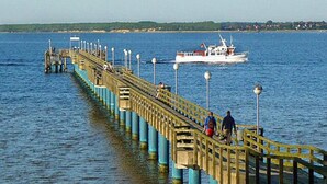 Un muelle que se adentra en una masa de agua, con un barco al fondo.