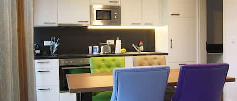 A modern kitchen with white cabinets, a microwave, and a dining area with a wooden table and two chairs.