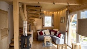 A wooden cabin interior with a sofa, chairs, a table, and a fireplace. - Amazing Chalet With hot tub (Sankt Georgen am Kreischberg)