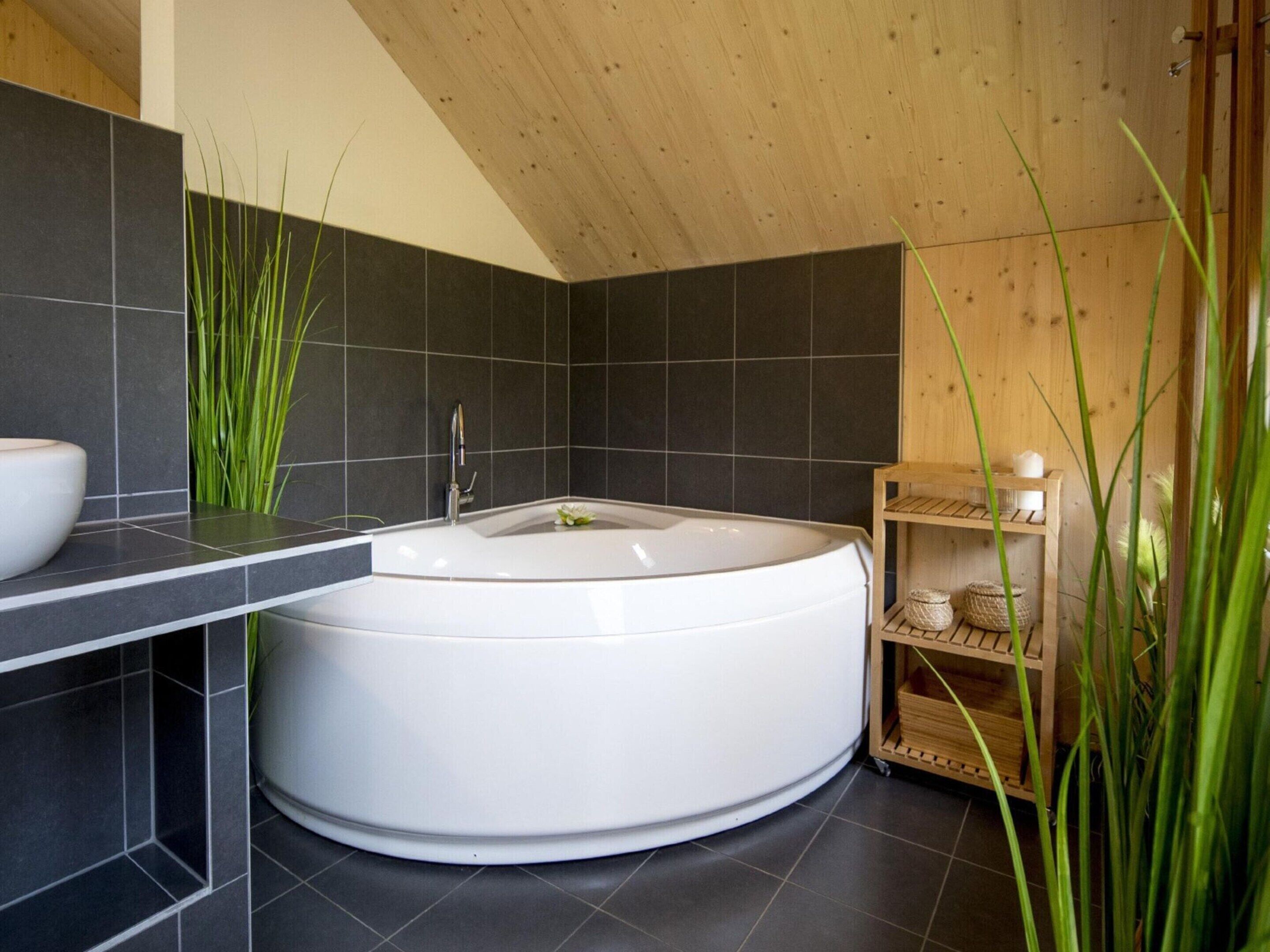 Ein modernes Badezimmer mit freistehender Badewanne, dunkel gefliesten Wänden und Holzboden.