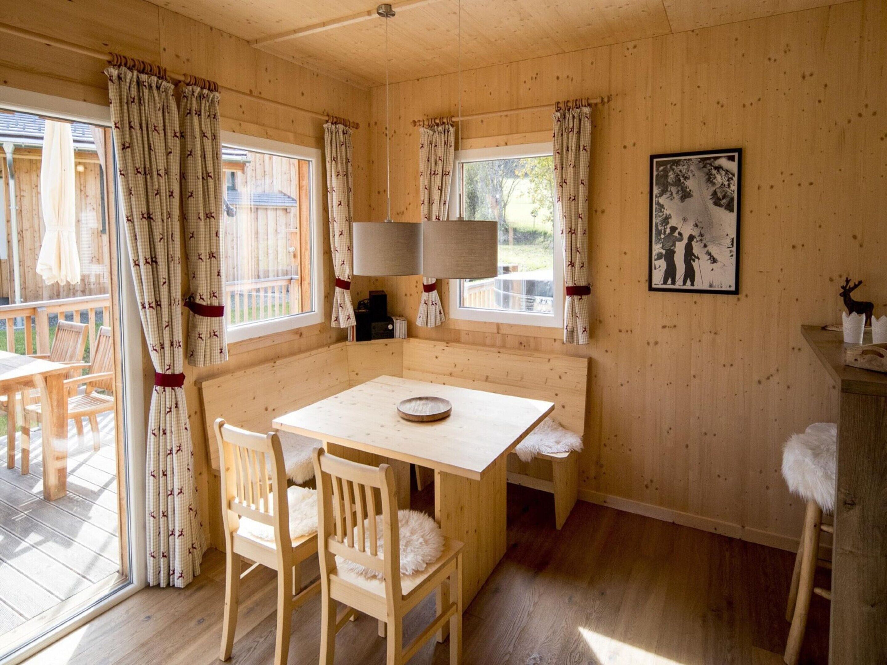 Interior acogedor de una cabaña con una mesa y sillas de madera, una lámpara y un cuadro en la pared.