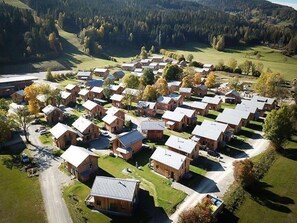 An aerial view of a residential area with multiple wooden houses arranged in a grid pattern, surrounded by green fields and trees. - Amazing Chalet With hot tub (Sankt Georgen am Kreischberg)