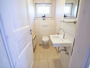 Une petite salle de bain étroite, avec des toilettes, un lavabo et une fenêtre située au-dessus des toilettes.