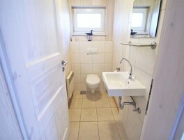 A small, narrow bathroom with a toilet, a sink, and a window above the toilet.