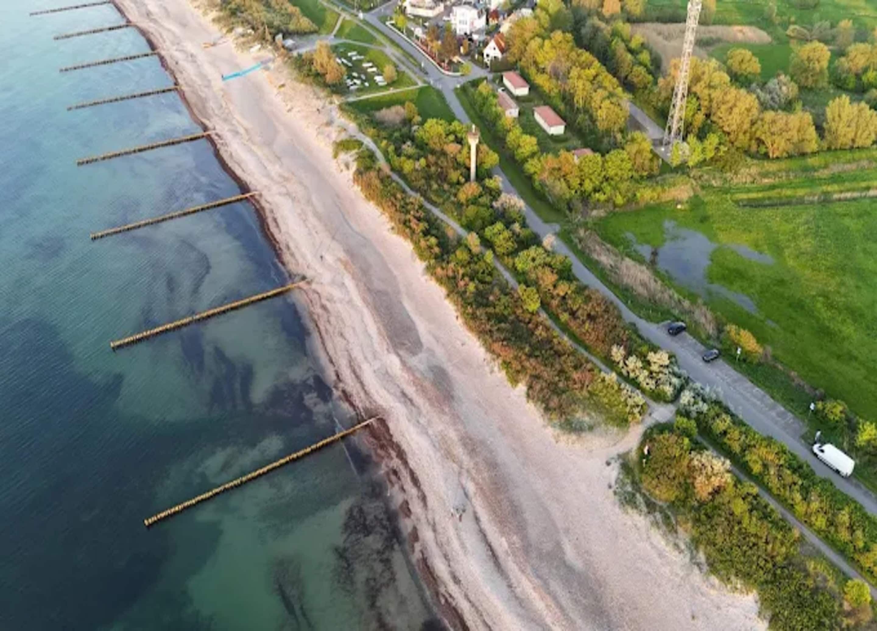 Una vista aerea di una zona costiera con spiaggia, una strada e edifici residenziali.
