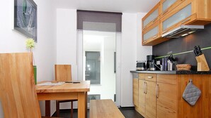 A compact kitchen with wooden cabinets, a countertop with kitchen appliances, and a dining area with a bench and chairs. - Appartementhaus Calmsailing, Borgerende (Boergerende-Rethwisch)