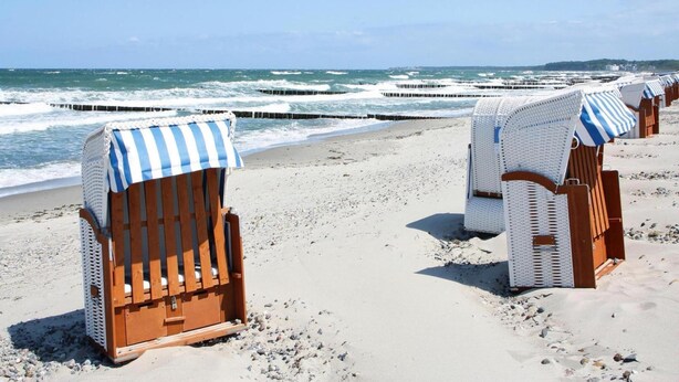 Beach chairs with striped covers on a sandy beach with the ocean in the background. - Appartementhaus Calmsailing, Borgerende (Boergerende-Rethwisch)